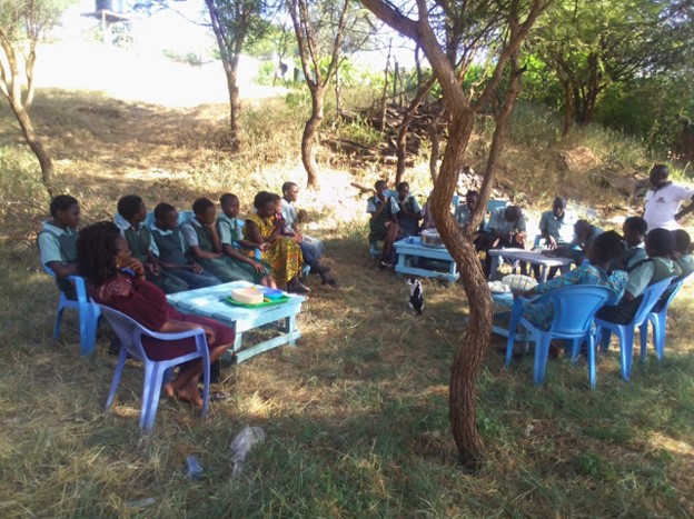 Group of adults and children attending a lecture in the countryside.