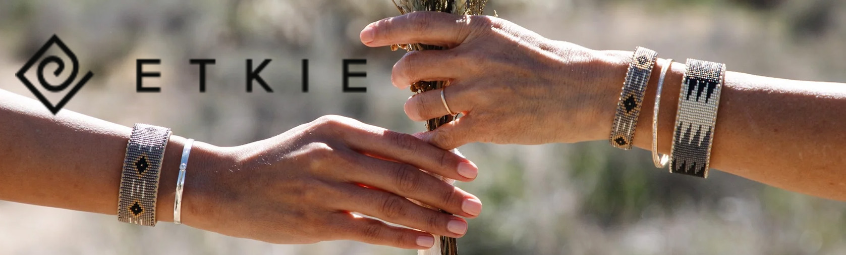 Photo of two hands grasping a bouquet of flowers. Each one is wearing an Etkie bracelet. 