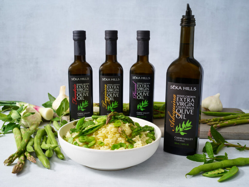 Photo of a bowl of risotto with four bottles of olive oil behind it. 