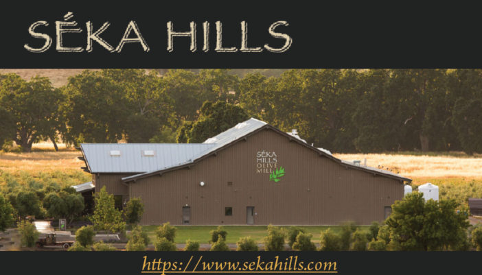 Photo of the Seka Hills property with vast green fields and olive groves, and a view of their building which displays the logo on the side. 