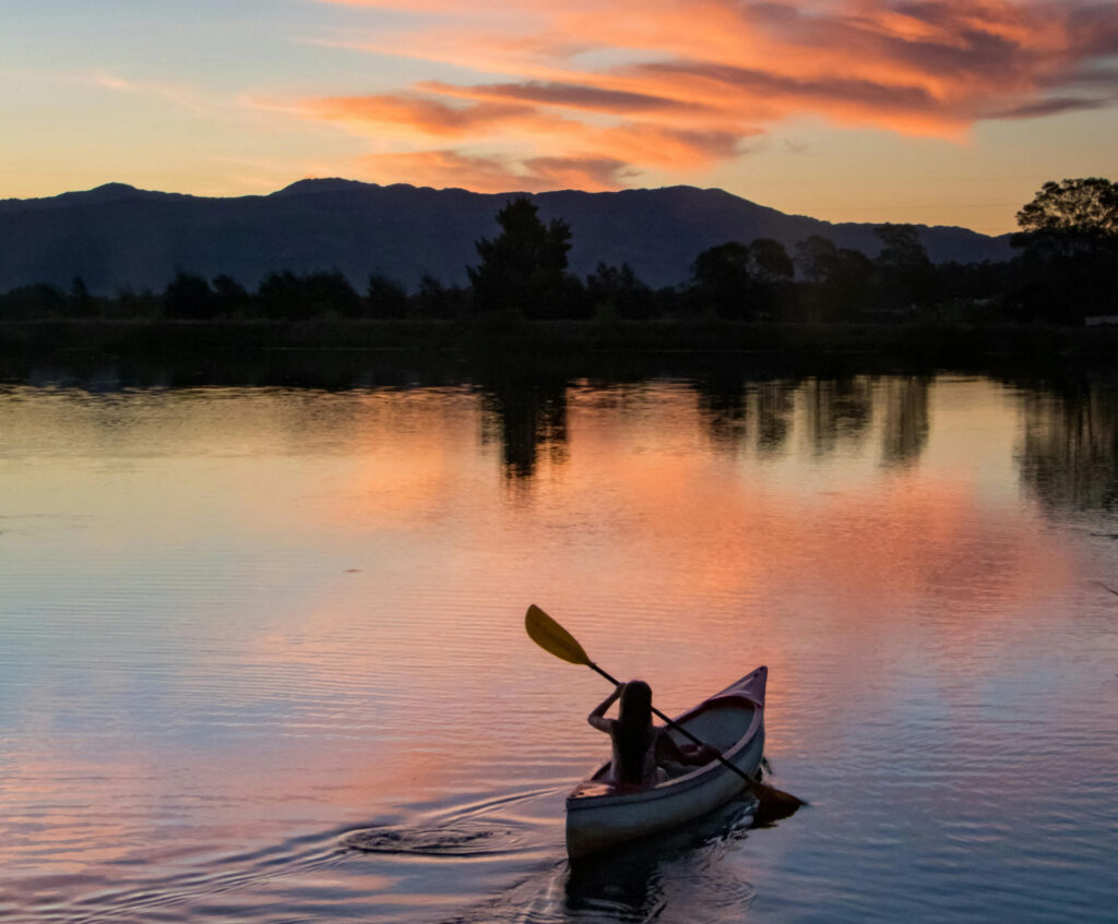 Photo of a person paddling a canoe across a lake at sunset. 